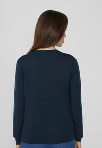 Suéter de punto azul marino con cuello redondo, mangas largas y puños y dobladillo con canalé. Textura suave, silueta ajustada.