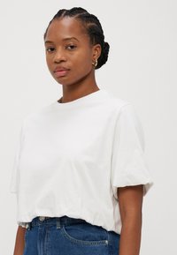 White cropped t-shirt, classic round neckline, short sleeves, soft cotton material, paired with high-waisted blue denim jeans.