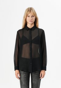 Svart gjennomsiktig skjorte med knapper og krage, lange ermer og en litt løstsittende passform. Stoffet ser lett ut med en glatt tekstur.