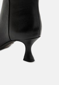 Zapato de tacón alto negro de cuero con un tacón afilado, textura suave y diseño elegante. Presenta detalles de costura a lo largo de las costuras.