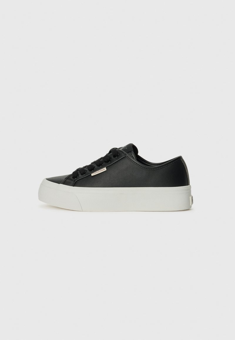 Black leather sneaker with a smooth texture, white rubber sole, round toe, and six black lace eyelets. Features a small metallic logo detail.