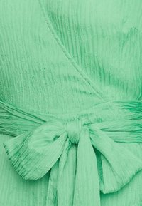 Zelené šaty s volným střihem vyrobené z texturované látky s vertikálními pruhy, stažené v pase detailem se zavázáním.