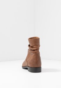 Bottine châtaigne en cuir avec un design effondré, bout arrondi et texture lisse. Présente un petit talon noir et une fermeture éclair à l'arrière.