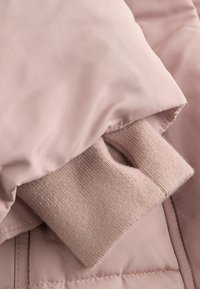 Polstret jakke i blødt pink materiale med en strikket manchet, der stikker frem under kraven, som fremhæver en glat tekstur og quiltet design.
