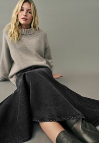 Grå strikket sweater med ribbede manchetter, parret med en sort denimnederdel med flared bund og mørke læderstøvler. Bløde teksturer.