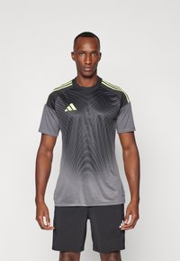 T-shirt de sport gris avec des accents noirs et des rayures jaunes sur les épaules. Présente un motif en vagues et des manches courtes. Assorti à un short noir.