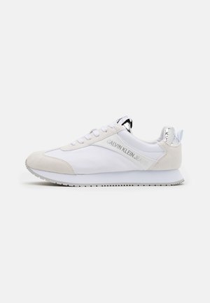 Hvid og beige lavtop sneaker med rund tå, snørelukning foran og sølv accenter på hæl og tunge, med "Calvin Klein Jeans" branding.
