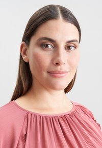 Blusa rosa antico in tessuto plissè, con scollo rotondo e morbidi drappeggi. Texture liscia e leggera, adatta per l'abbigliamento casual.