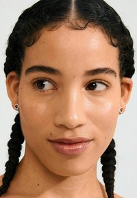 Pendientes de studs redondos con un centro negro, rodeado de un borde metálico plateado. Acabado suave y diseño minimalista. El modelo tiene el cabello trenzado.
