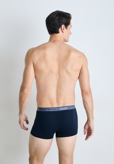 Mørkeblå boksershorts med en grå midjebånd som har "EMPORIO ARMANI" logo. Stoffet ser glatt og tett sittende ut, noe som fremhever en strømlinjeformet design.