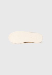 Sole of light beige shoe featuring floral and leaf patterns embossed on the outsole, shown against a plain background.