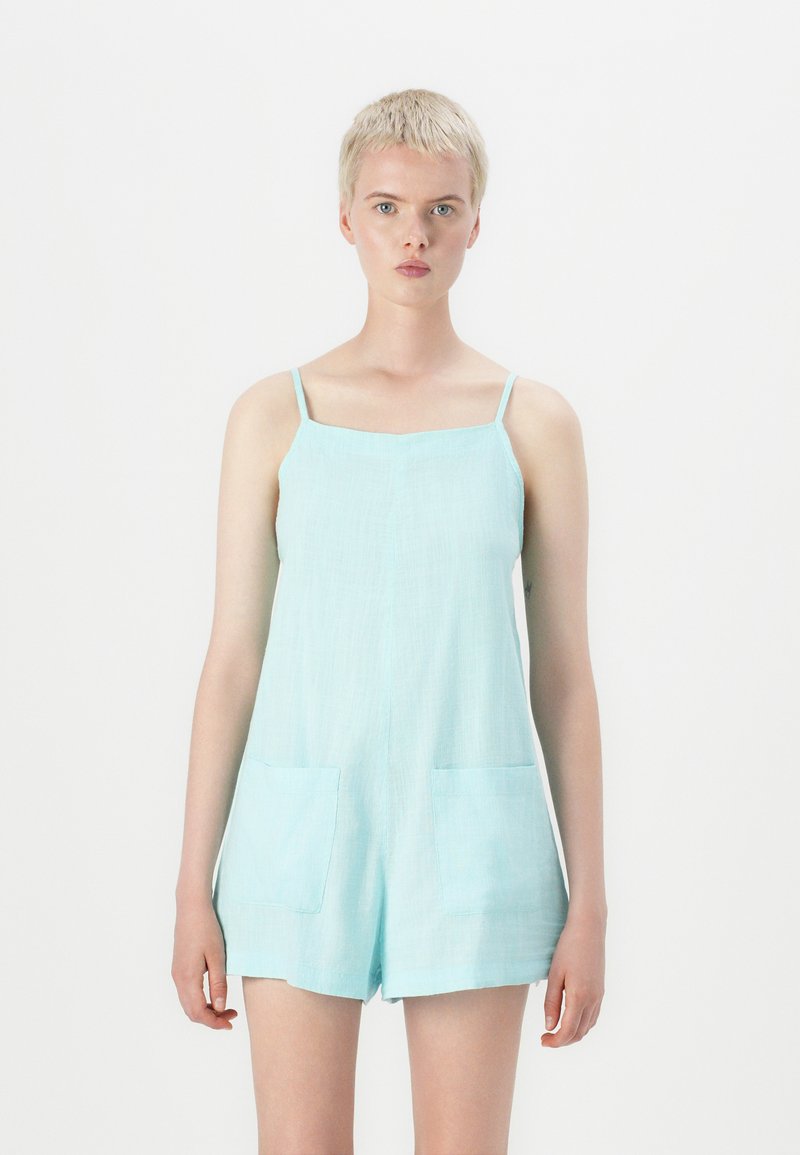 Rompers en lin bleu clair avec des fines bretelles, un décolleté carré et deux poches avant. Présente une coupe ample et une texture douce.