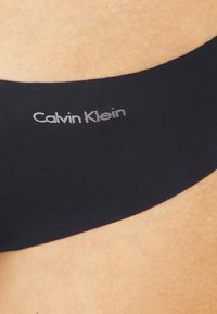 Sous-vêtement noir Calvin Klein avec une texture lisse, arborant un logo subtil en argent, mettant en avant un design minimaliste.