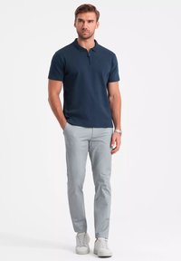 Granatowa koszulka polo z zamkiem na ćwierć, w połączeniu z jasnoszarymi spodniami i białymi trampkami. Gładka faktura i dopasowany krój.