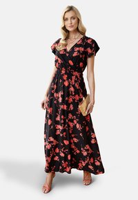 Maxikleid in Schwarz mit rotem Blumenmuster. Mit kurzen Ärmeln, einer taillierten Taille und einer fließenden Silhouette. Wird mit einer goldenen Clutch kombiniert.