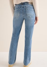 Jeans de denim azul claro con un diseño de pierna recta, bolsillos traseros con parche y una textura sutilmente descolorida. Disponible en longitud hasta el tobillo.