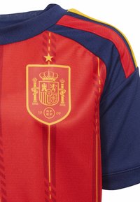 Červené a námornícke športové dresy so žltými a červenými pruhmi, s žltým erbom národného futbalového tímu Španielska na hrudi.