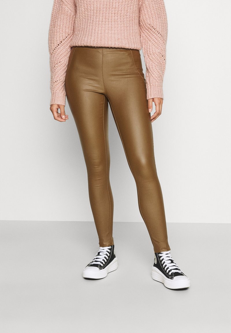 Leggings in finta pelle color crema con vita alta, abbinati a un maglione rosa lavorato a maglia e sneakers platform nere con suola bianca.