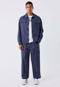 Marineblauwe zip-up jacket met twee borstzakken, gecombineerd met bijpassende losse broek. Draagt over een wit T-shirt en gestyled met sneakers.