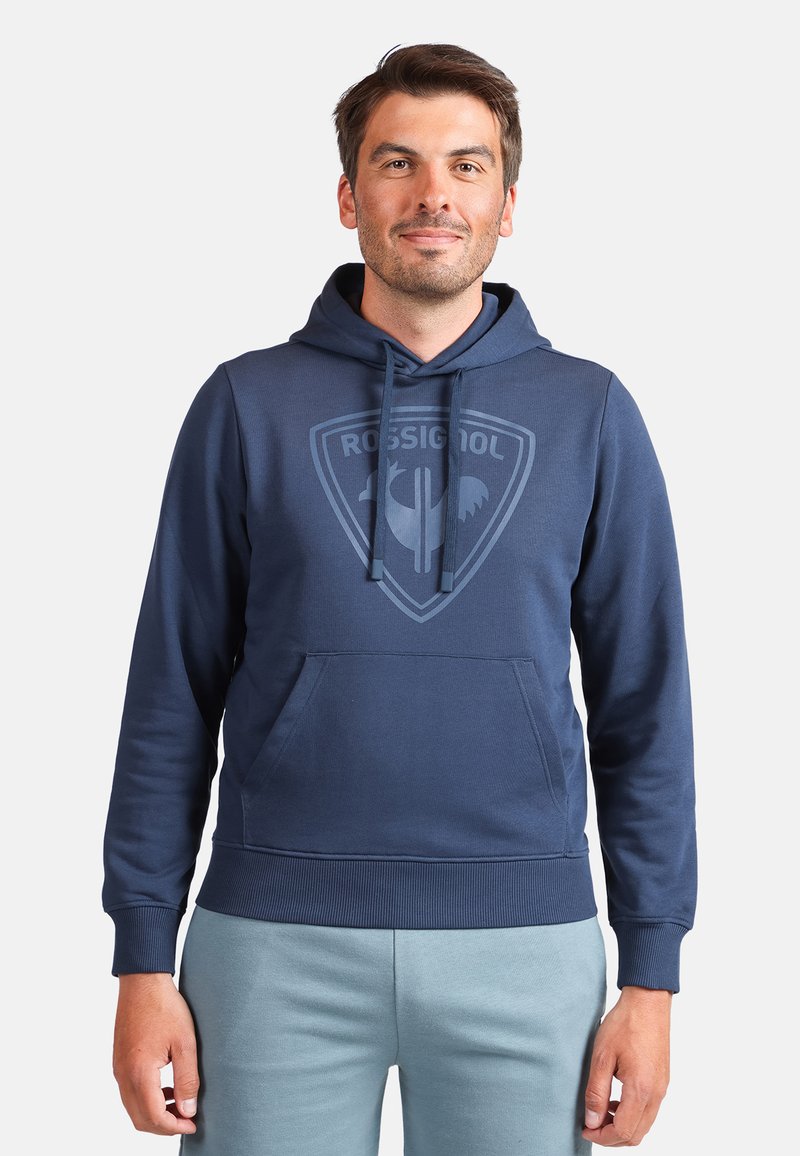 Tmavě modrá mikina s kapucí a klokaní kapsou. Má tónovaný logo motiv na hrudi a žebrované manžety a lem.