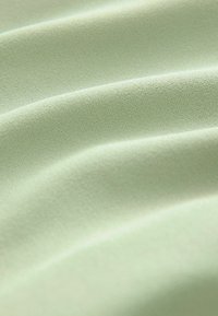 Vaaleanvihreä kangas, jossa on pehmeä ja sileä pinta, esitellen kevyitä poimuja ja hienovaraisen kiillon. Ihanteellinen vaate- tai verhoilukäyttöön.