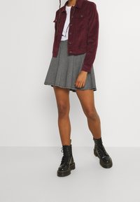 Chaqueta de pana burdeos, camiseta blanca, falda de cuadros con pliegues y botas negras con cordones y suelas de plataforma. Tejidos texturizados y patrones contrastantes.