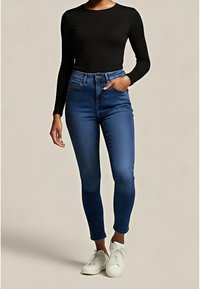 Tmavě modré džíny s vysok ým pasem a úzkým střihem, se pěti kapsami a předním zapínáním na knoflíky, doplněné černým tričkem s dlouhým rukávem a bílými teniskami.