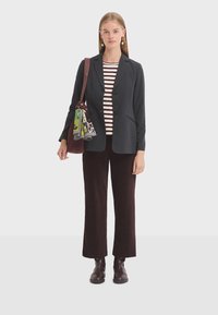 Woman wearing dark blazer, striped shirt, dark corduroy pants, and boots, carrying a brown shoulder bag with a colorful scarf attached.