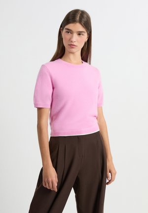 Short-sleeve pink knit sweater with a round neckline, featuring a soft texture and a cropped design, paired with high-waisted brown trousers.