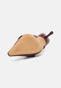 Chaussure à talon haut bordeaux avec un bout pointu, dessus en cuir verni lisse et semelle en caoutchouc beige texturée avec des rainures horizontales pour une meilleure adhérence.