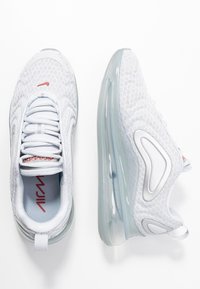 Vita idrottsskor i vitt med meshnät, vadderad krage, genomskinlig luftkuddingsula, silverdetaljer och röd logotyp.