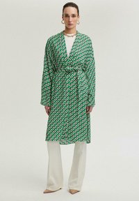 Roheline mustriline kimono-stiilis rüü, millel on pikad varrukad ja enda kinni sidumise vöö, kihiliselt valge üleriietuse ja laia jala kreemivärvi pükste kohal.