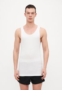 White sleeveless tank top in a fitted design, made of lightweight cotton. Features a round neckline and slightly textured finish.