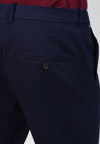 Granatowe spodnie o gładkiej fakturze, z zapinaną na guzik tylną kieszenią i szlufkami na pasek. Krój jest dopasowany i prosty.