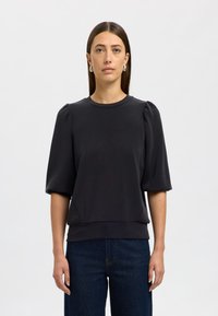 Melnā džemperis ar īsām, puffed piedurknēm un apaļu kakla izgriezumu. Gluda auduma ar brīvu piegriezumu, ar apakšmalu, kas atrodas jostas vietā.