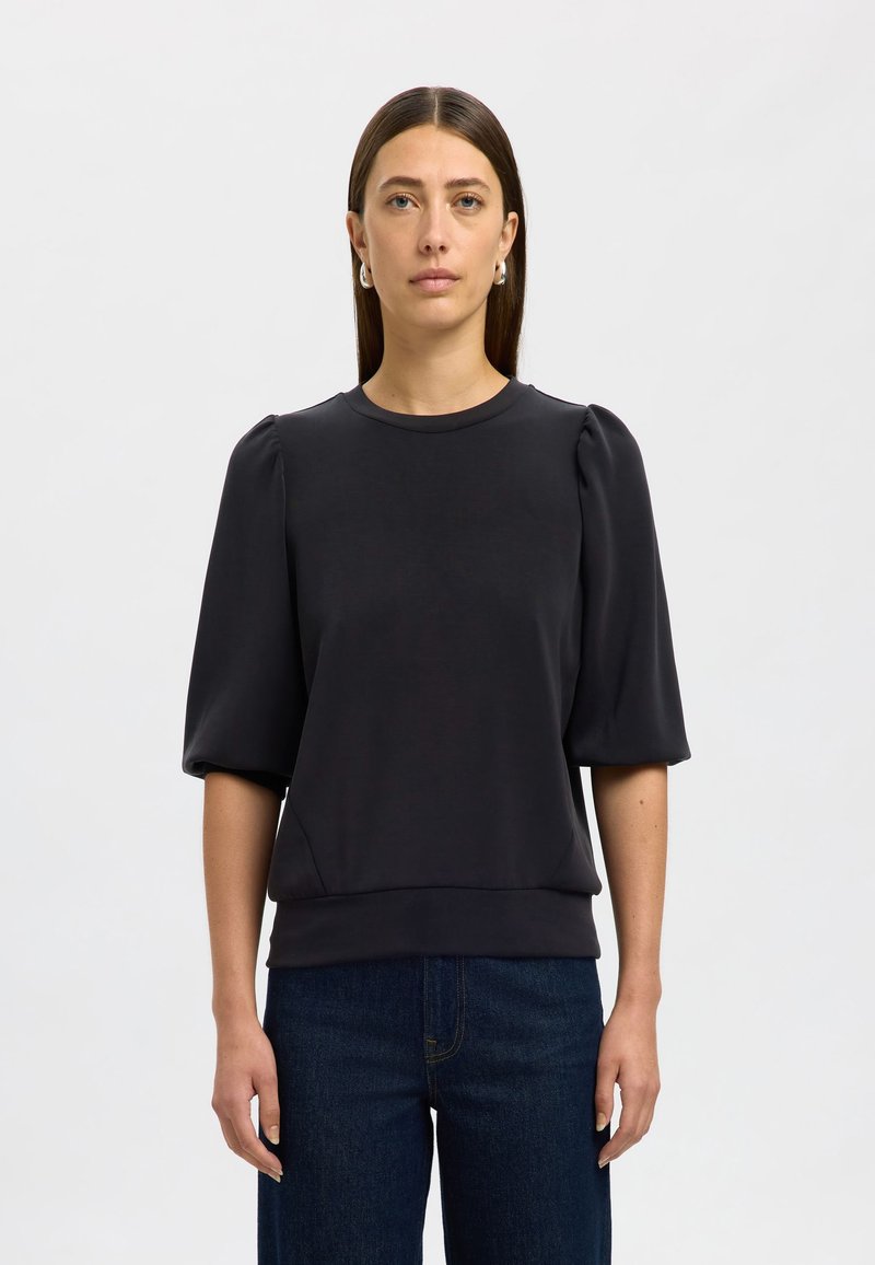 Melnā džemperis ar īsām, puffed piedurknēm un apaļu kakla izgriezumu. Gluda auduma ar brīvu piegriezumu, ar apakšmalu, kas atrodas jostas vietā.