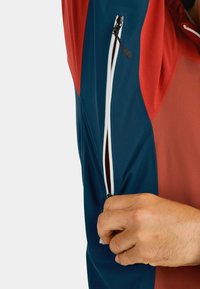 Colorful jacket featuring a blend of dark blue and red panels. Includes a white zipper detail on the sleeve with a pull tab. Smooth texture.