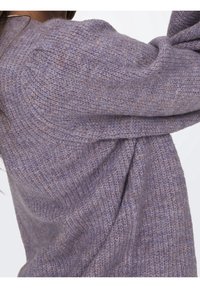 Lila stickad tröja med en texturerad design och avslappnad passform, synliga stygn och uppvikta ärmar. Mjuk, varm material.