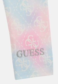 Tkanina u pastelnim bojama s uzorkom dijamanta, sa bijelim logotipom. Logotip "GUESS" u srebrnom sjaju na donjem dijelu. Mekana tekstura.