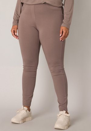Braune stretchleggings met een aansluitend ontwerp, platte naden en enkelmanchetten, gecombineerd met lichtgekleurde sneakers.