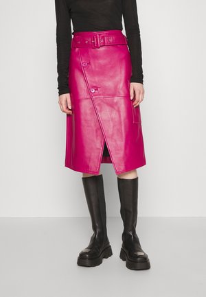 Fuksjowa skórzana spódnica owijana z paskiem w talii, ukośnymi guzikami z przodu i bocznymi kieszeniami, zestawiona z czarnymi kozakami sięgającymi do kolan.
