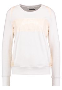Sudadera crema clara de manga larga, con un escote redondo y un panel de tejido brillante en el pecho que presenta una marca en relieve.