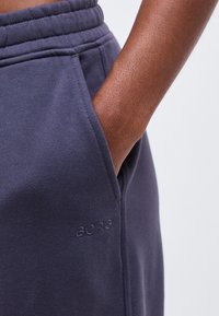 Άτομο με σκουρόχρωμο δέρμα που φορά ναυτικό μπλε φόρμα παντελόνι με το χέρι στην πλαϊνή τσέπη και μικρό λογότυπο "BORG" κεντημένο κάτω από την τσέπη.