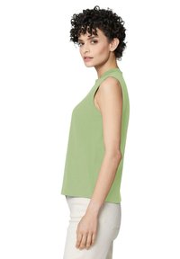 Lichtgroene mouwloze top met een hoge halslijn en een zachte textuur, gecombineerd met lichtgekleurde, aansluitende broek. Eenvoudig ontwerp, zonder patronen.