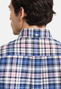 Kariertes Hemd mit blauen, weißen, pinken und schwarzen Karos. Kurzarm, Button-Down-Kragen und ein einzelner Rückenfalte. Aus Baumwollstoff.