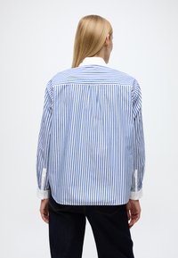 Camicia a righe blu e bianche con colletto bianco, maniche lunghe e dettaglio con pince sul retro. Realizzata in tessuto leggero con una vestibilità comoda.