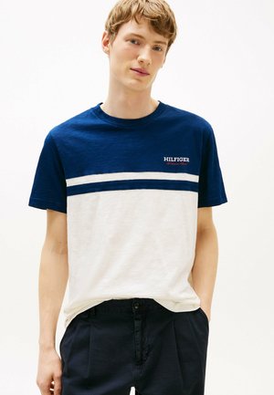 Marineblå og hvid bomulds t-shirt med vandrette striber; prydet med "HILFIGER" logo i rødt på brystet. Korte ærmer og rund halsudskæring.