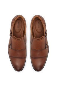 Zapatos marrones de cuero sin cordones con una textura suave, que presentan hebillas decorativas y detalles de costura. El interior está forrado para mayor comodidad.