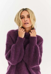 Fialový oversized sveter s vysokým golierom, vyrobený z mäkkého, nadýchaného materiálu, s širokými rukávmi a voľným strihom.