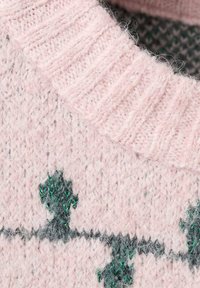 Stickad rosa tröja med en ribbad krage, prydd med gröna och grå trädmönster. Mjuk textur med ett fluffigt och varmt utseende.